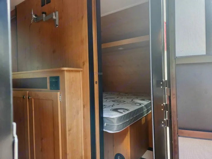 Cozy RV rental interior featuring a comfortable bed, storage cabinet, and TV mount for your travel comfort.. Riverside Rv Retro 2023