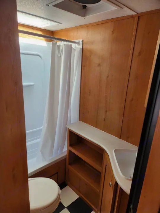 RV rental: compact bathroom with shower, toilet, sink vanity, and checkered floor, designed for travel convenience.. Riverside Rv Retro 2023