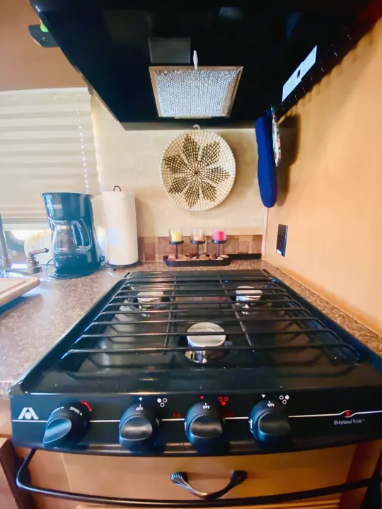 RV rental kitchen view: A black gas stove is central, with a coffee maker, paper towels, and decorative basket visible.. Forest River Coachmen Prism 2014