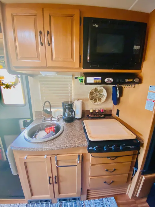 Compact RV rental kitchen with sink, microwave, stovetop, and storage. Perfect for travel cooking.. Forest River Coachmen Prism 2014