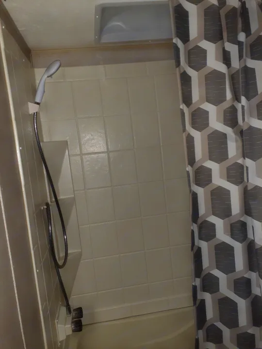 Compact shower and tub in an RV rental, with a handheld showerhead, light-colored walls, and a modern patterned curtain.. Forest River Coachmen Catalina Summit 2020