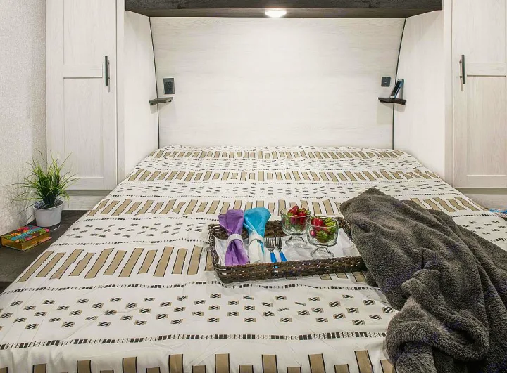 Cozy RV rental bedroom: bed with patterned bedding, breakfast tray with fruit, and soft blanket for relaxing travel.. Sportsmen SE 2023