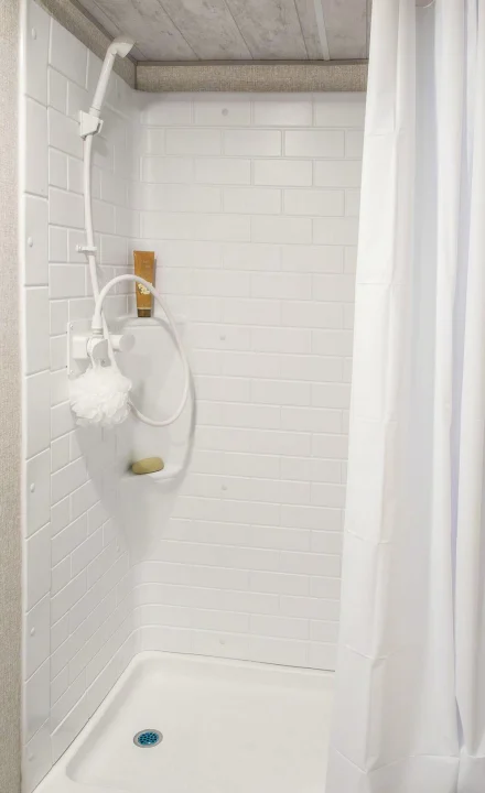 Bright white shower stall in an RV rental, with a handheld showerhead, loofah, and soap. Features a modern, subway tile-like design.. Sportsmen SE 2023