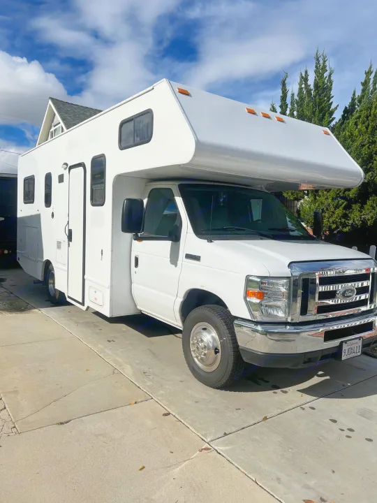 Explore with this clean white RV rental, parked on a concrete driveway under a blue sky. Ready for adventure.. Thor Majestic 2019