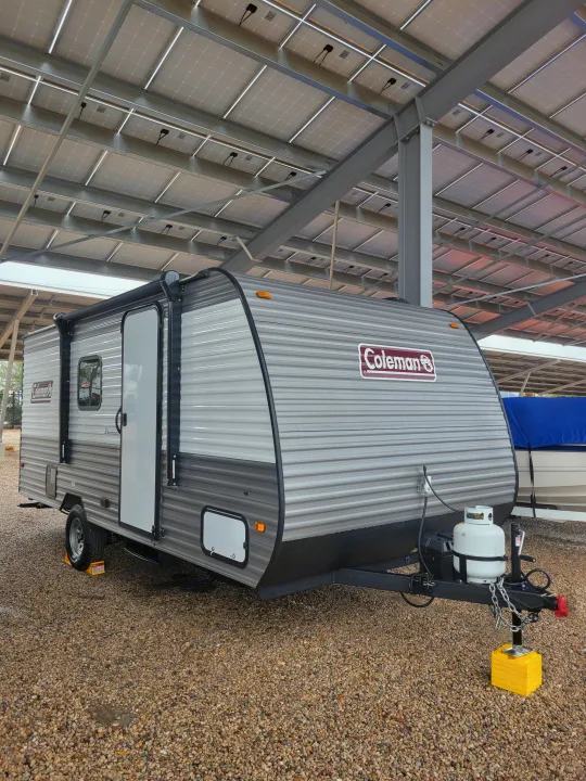 Coleman travel trailer RV rental parked on gravel under a solar panel roof. Ideal for secure outdoor storage.. Coleman Coleman Lantern 17B 2024