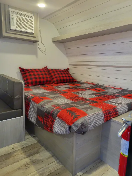 This RV rental offers a compact sleeping area with a cozy plaid quilt, bench seating, and a wall-mounted AC unit.. Coleman Coleman Lantern 17B 2024