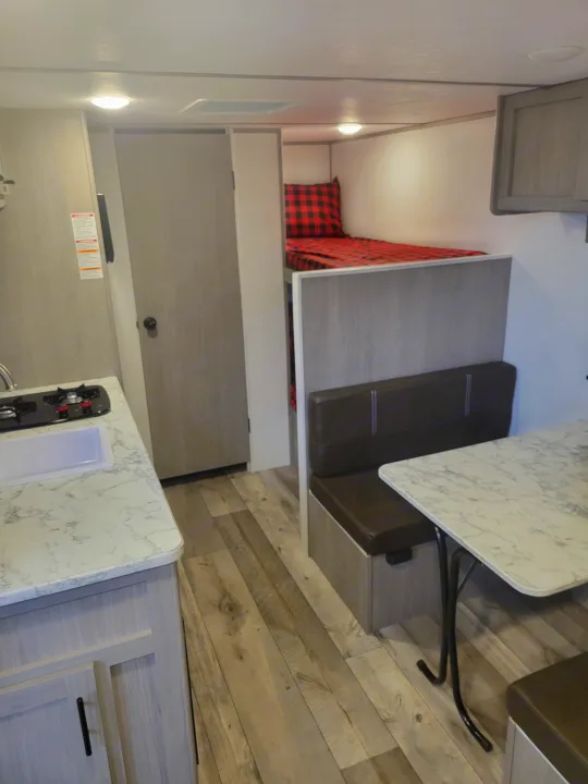 Spacious rv rental interior features a kitchenette, cozy bunk beds with red plaid, and a dinette area with brown seating.. Coleman Coleman Lantern 17B 2024