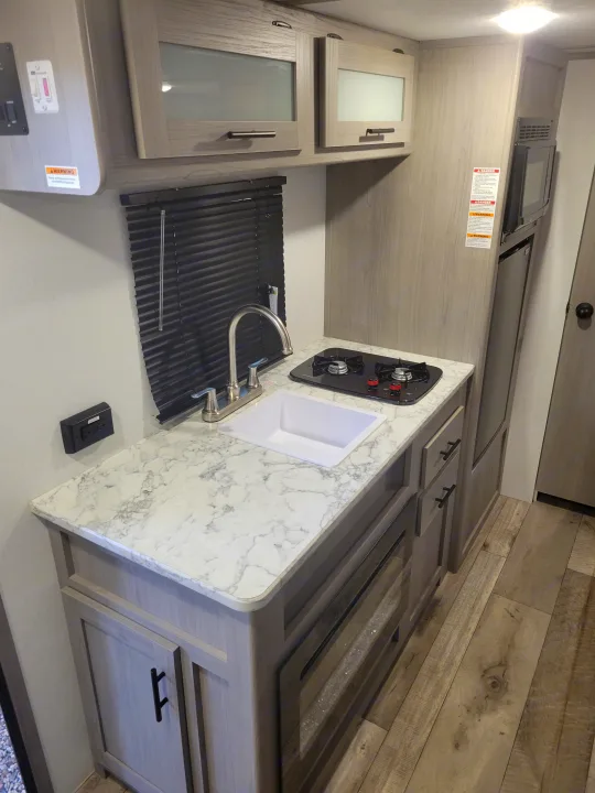 Compact RV rental kitchen features sink, stovetop, microwave, and cabinets. Ideal travel trailer interior.. Coleman Coleman Lantern 17B 2024