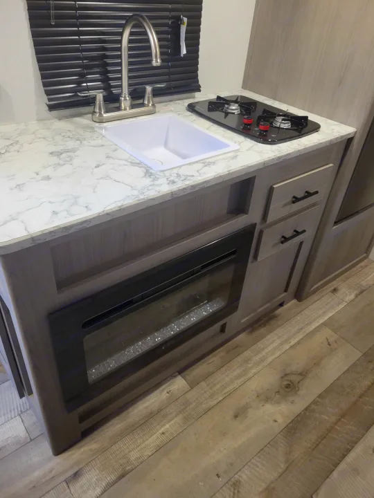 RV rental kitchenette: sink, 2-burner cooktop, marble-look counter, electric fireplace, & wood floor.. Coleman Coleman Lantern 17B 2024