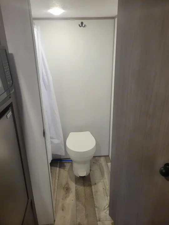 RV rental's compact bathroom features a white toilet, shower curtain, and light wood-look floor. Functional interior for travel.. Coleman Coleman Lantern 17B 2024