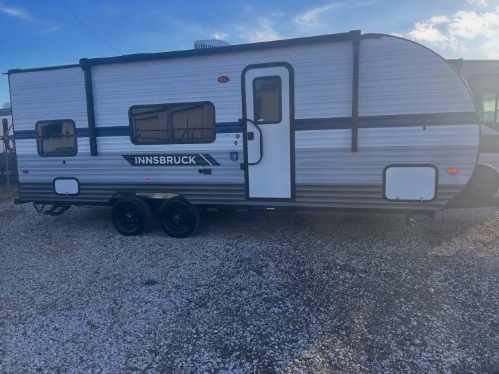 Grey Innsbruck travel trailer parked on a gravel lot, ready for your next rv rental adventure under a clear sky.. Gulf Stream Ameri-Lite 2022