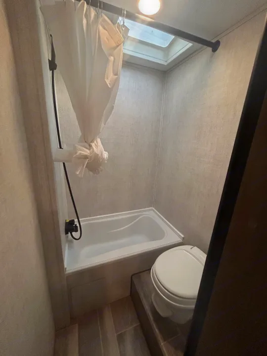 View inside an RV rental bathroom, showing a small bathtub with shower, a toilet, and a skylight for natural light.. Gulf Stream Ameri-Lite 2022