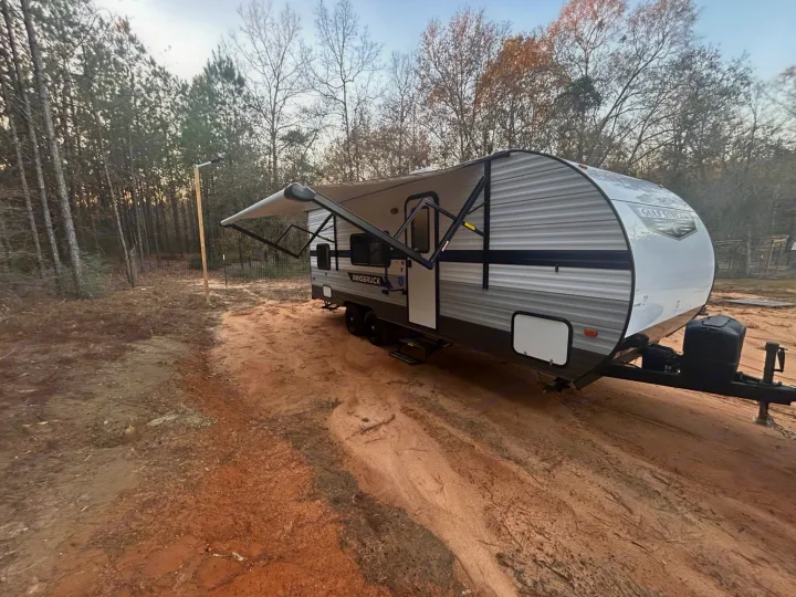 RV rental: Gulf Stream Innsbruck travel trailer with awning out, parked on dirt site surrounded by pine and deciduous trees.. Gulf Stream Ameri-Lite 2022