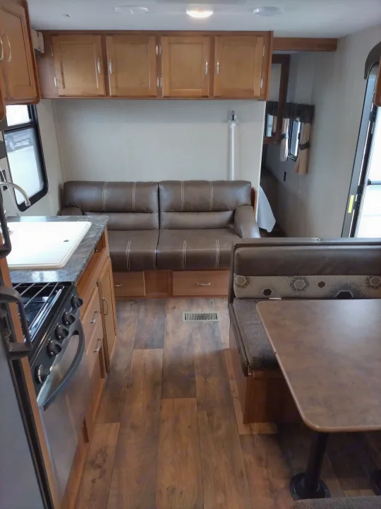 Inviting RV rental interior showcasing a kitchen with stove/sink, comfy sofa, and dinette, all on wood-look flooring.. Keystone RV Springdale Eco-Lite 2018