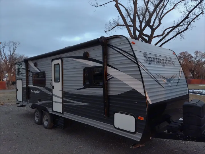 Side view of a grey and black Springdale travel trailer, ready for your RV rental. Parked outdoors with trees.. Keystone RV Springdale Eco-Lite 2018
