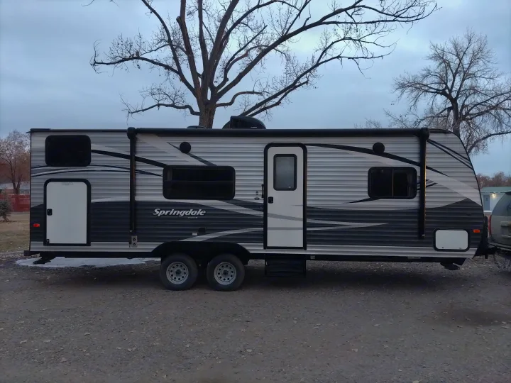 Spacious Springdale travel trailer, a gray and white RV rental, parked on a gravel lot under a cloudy sky.. Keystone RV Springdale Eco-Lite 2018