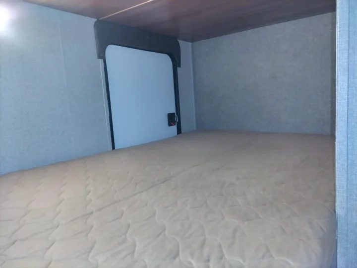 Cozy RV rental sleeping space with quilted mattress, light gray walls, and small rear door.. Keystone RV Springdale Eco-Lite 2018