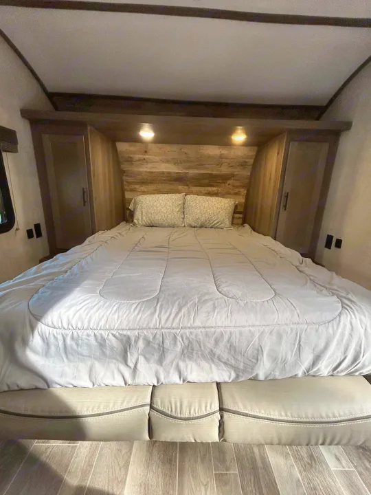 RV rental interior: a cozy bedroom with a comfortable bed, wood headboard, lighting, and side cabinets. Great for trips.. Gulf Stream Ameri-Lite 2022