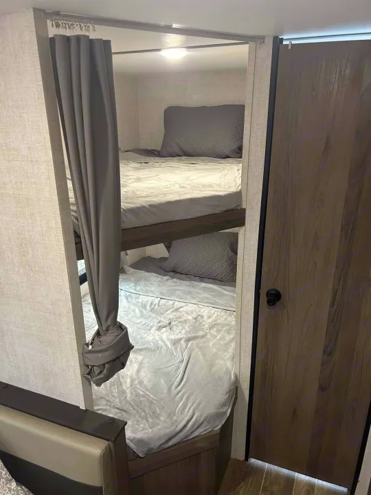 RV rental bunk beds: a compact sleeping area with a gray privacy curtain and two comfortable beds. Perfect for families.. Gulf Stream Ameri-Lite 2022
