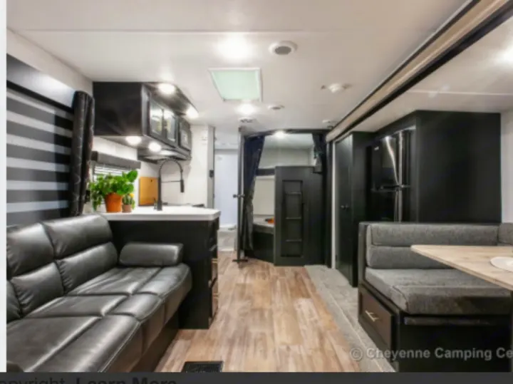 Spacious RV rental interior with black sofa, modern kitchen, and dining booth. Perfect for adventures.. Forest River Cherokee 2022