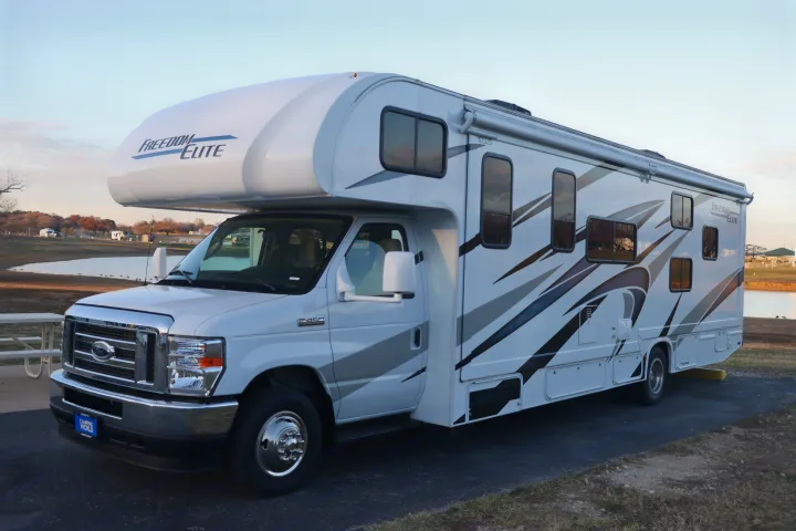 Spacious Freedom Elite RV rental (Class C motorhome) parked by a lake, ideal for travel adventures.. Thor Freedom Elite 2023