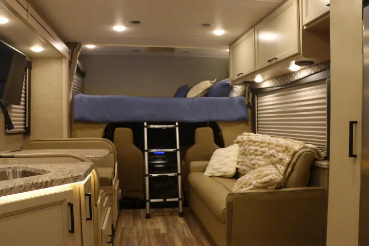 Modern RV rental interior: well-lit space with kitchen, dinette, overhead bed, and plush sofa for comfortable travel.. Thor Freedom Elite 2023