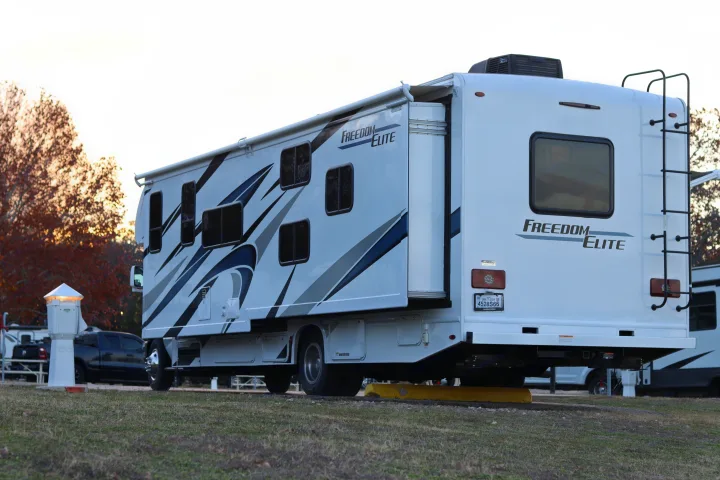 White Freedom Elite motorhome RV rental, with its slide-out extended, parked at a campsite.. Thor Freedom Elite 2023