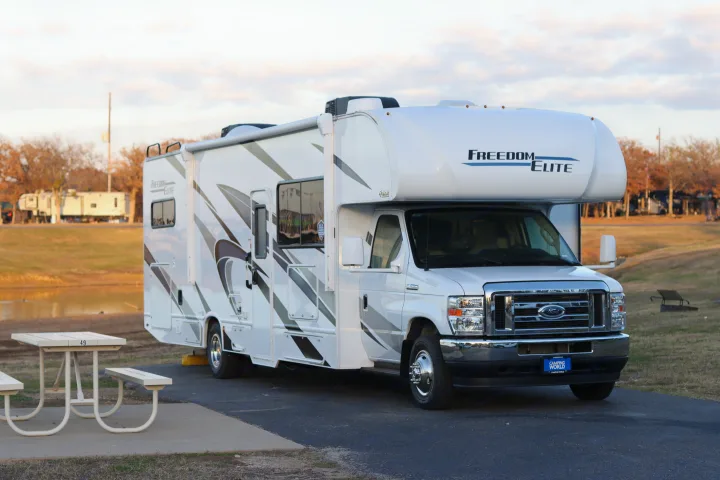 A white Freedom Elite Class C RV rental is parked at campsite 49 next to a picnic table, ready for your camping travels.. Thor Freedom Elite 2023