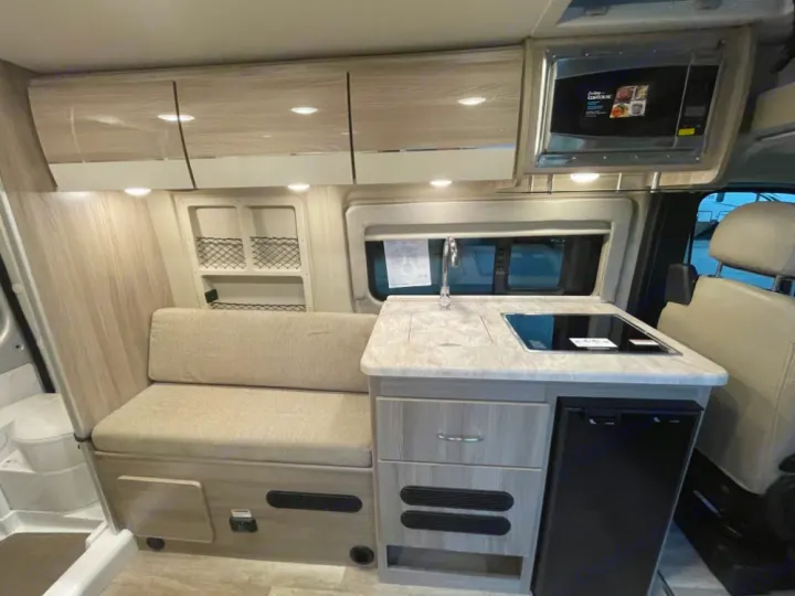 Compact RV rental interior featuring a modern kitchenette with sink, stovetop, fridge, microwave, and cozy bench seating.. Thor Scope 18G 2024