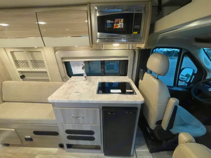 Compact RV rental interior with kitchen (microwave, sink, stovetop, fridge) & cozy bench seating.. Thor Scope 18G 2024