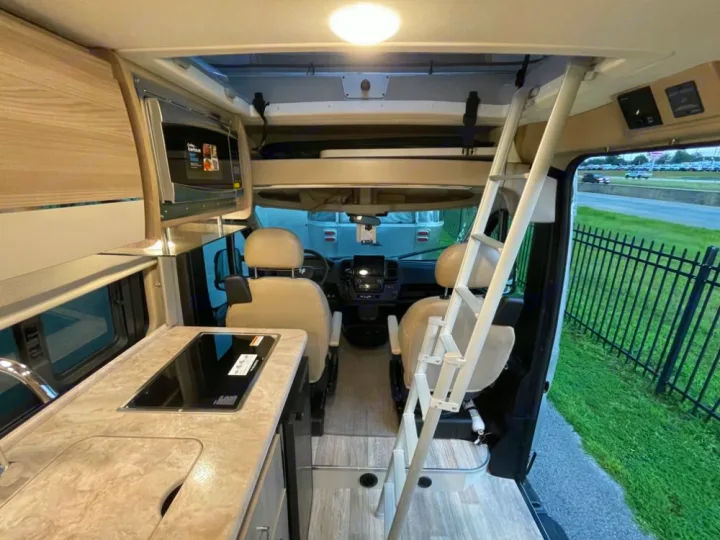 Inside an RV rental: kitchen counter with sink/stovetop, microwave, and ladder to a sleeping bunk.. Thor Scope 18G 2024