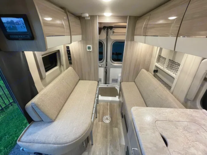 Spacious RV rental interior showing two comfy bench seats, overhead storage, and a control panel. Perfect for your next adventure.. Thor Scope 18G 2024