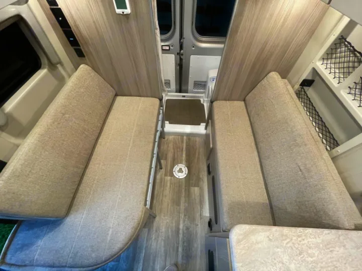View inside an RV rental: two long, upholstered benches face each other over wood-look flooring. Ready for travel or relaxation.. Thor Scope 18G 2024