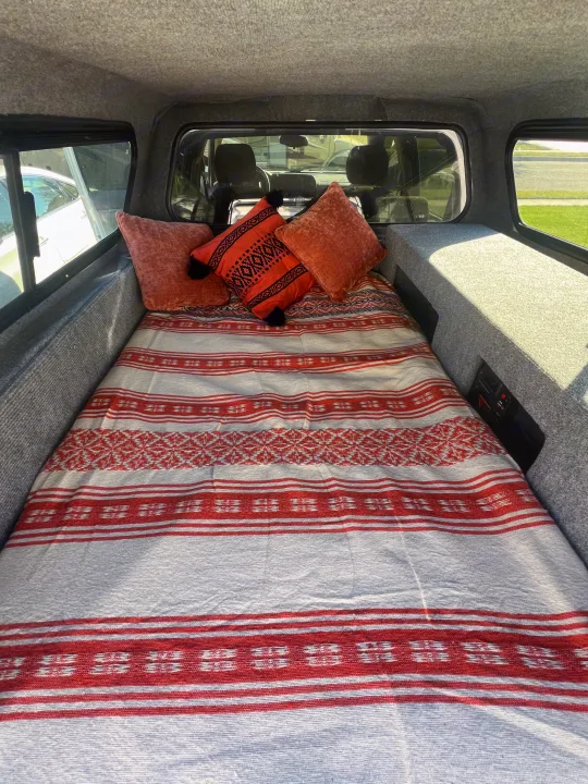Cozy truck camper interior with a bed, red blanket, pillows, and built-in storage. Ideal for RV rental road trips.. Chevrolet Silverado 1500 2009