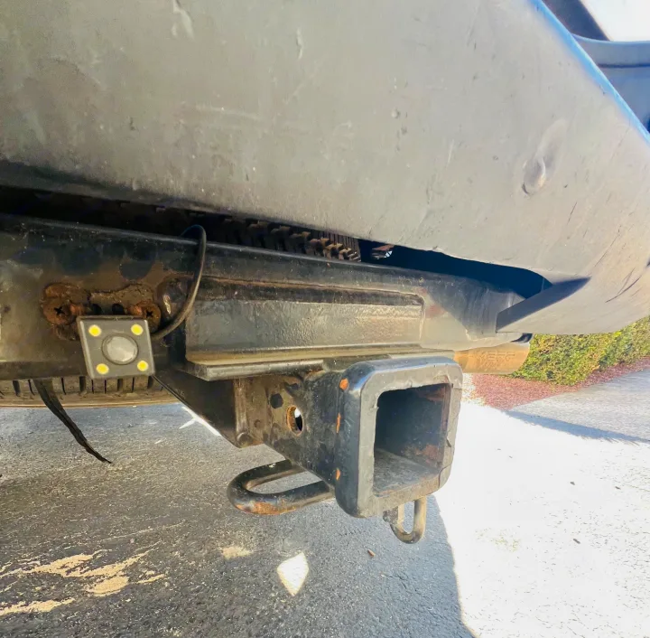 Looking up at an RV rental's rear: a rusty tow hitch with an attached backup camera, its LEDs illuminated. Paved ground below.. Chevrolet Silverado 1500 2009