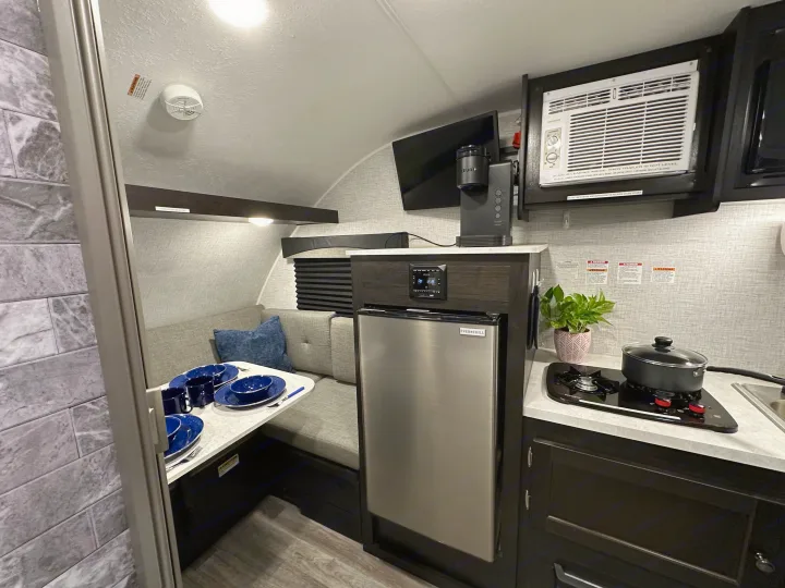 This RV rental interior features a compact kitchen with an Ever Chill fridge, stove, Keurig, and a cozy dinette.. Braxton Creek Bushwhacker Plus 2022