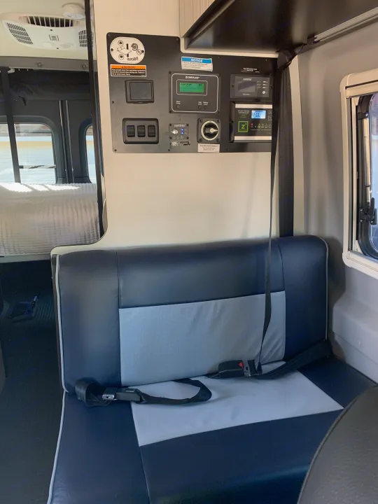 RV rental interior: A detailed view of the RV's control panel, showing power, water, and solar readouts, next to comfortable seating and a bed.. Winnebago Revel 2022