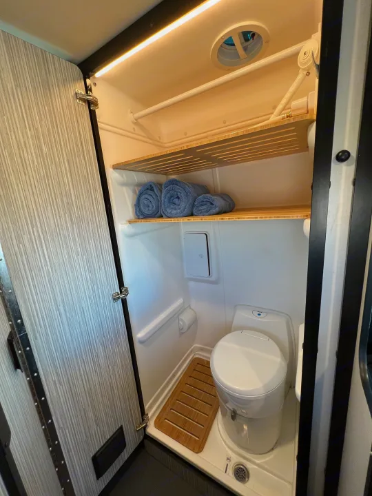 RV rental wet bath: toilet, shower pan, bamboo shelves with towels, overhead light & vent. Compact & functional.. Winnebago Revel 2022