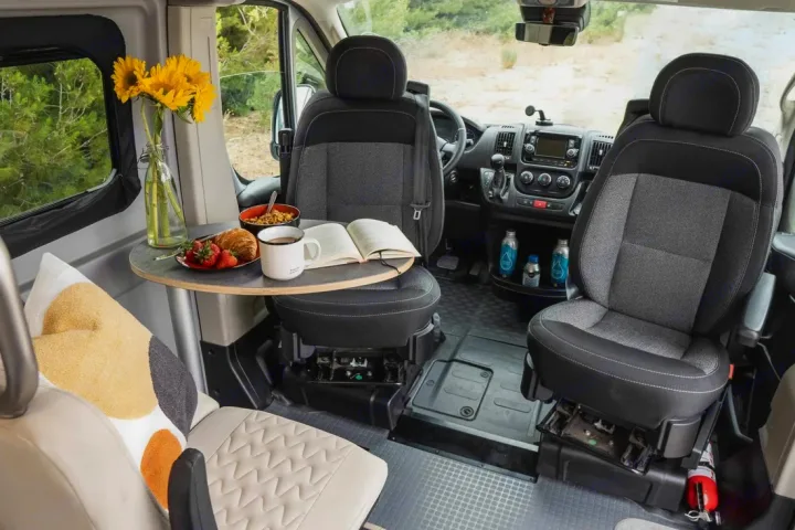 Swivel seats and a table set for breakfast with sunflowers and a book inside an RV rental camper van.. Winnebago Solis 2022