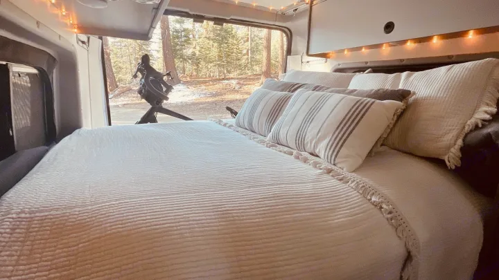 Cozy RV rental interior: bed with pillows facing a snowy forest view & bike outside. Ideal for travel.. Winnebago Solis 2022