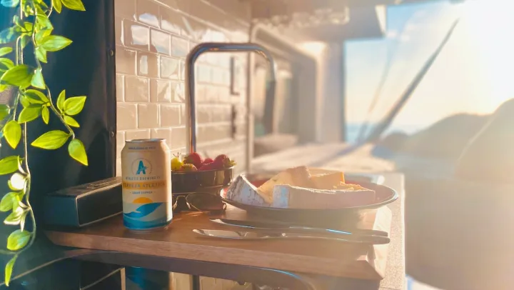 Cozy RV rental interior with a non-alcoholic beer, cheese, and fruit, bathed in golden hour light. Travel bliss!. Winnebago Solis 2022