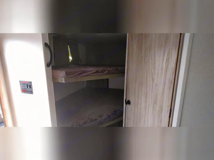 Inside an RV rental: two bunk beds with mattresses, a control panel on the wall, and a light-colored wood door, ideal for travel.. Winnebago 2301BHS 2022