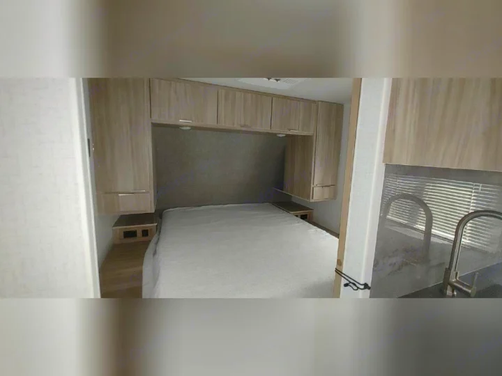 Cozy RV rental interior showcasing a bedroom with overhead storage, a comfortable bed, and a small kitchen area.. Winnebago 2301BHS 2022