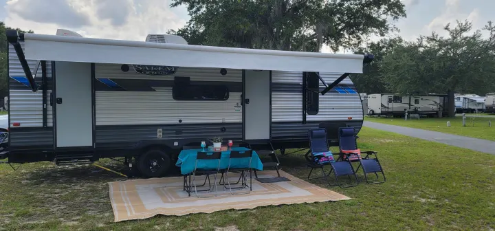 This RV rental offers a comfortable campsite setup with an awning, outdoor dining area, and lounge chairs on a mat.. Forest River Salem Cruise Lite 2021