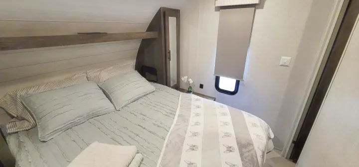 Comfortable RV rental bedroom: cozy bed, light wood headboard, mirrored cabinet, and small window.. Forest River Salem Cruise Lite 2021