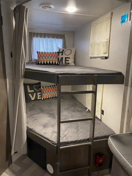 Cozy RV rental bunk beds, perfect for families. Features comfy grey bedding, pillows, and a ladder in the compact interior.. Forest River Salem Cruise Lite 2021