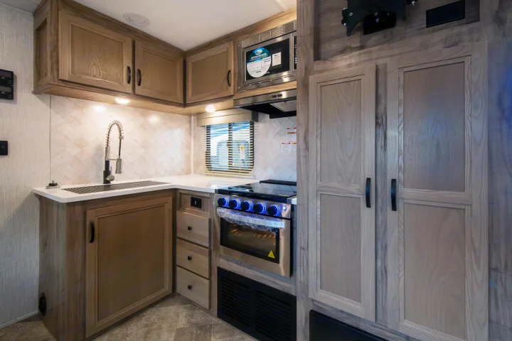 Explore this clean, modern RV kitchen with a sink, microwave, and oven, ideal for your rv rental trips.. Palomino Solaire Ultra Lite 2023