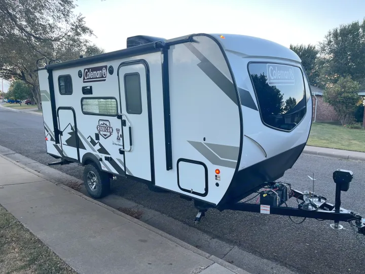 White & black Coleman Rubicon travel trailer, perfect for an rv rental adventure, parked on a suburban street.. Dutchmen Coleman Rubicon 2022