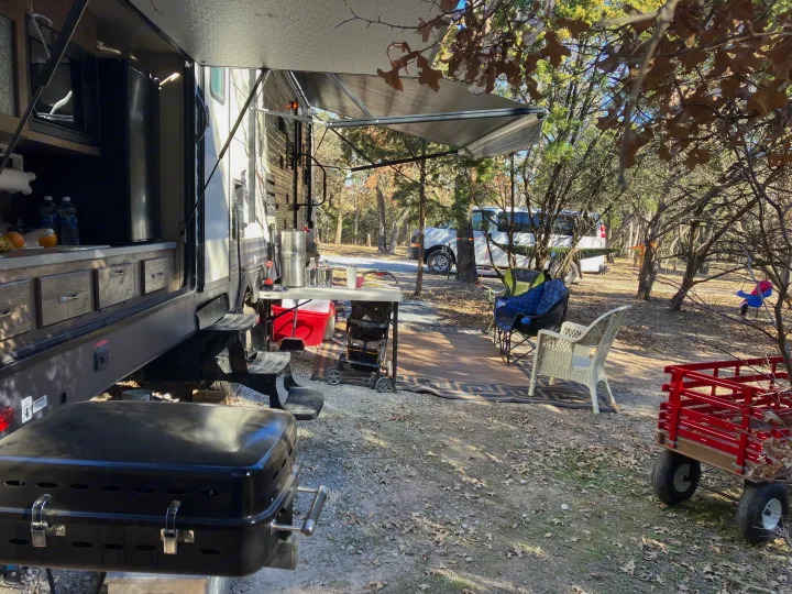 This RV rental shows a full outdoor kitchen, shaded seating area, and grill at a cozy wooded campsite.. Forest River Palomino Puma 2018