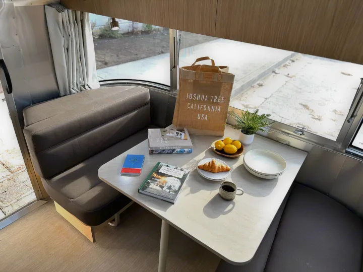 Bright RV rental interior featuring a dinette table with breakfast, books, and a Joshua Tree tote bag.. Airstream Flying Cloud 2017